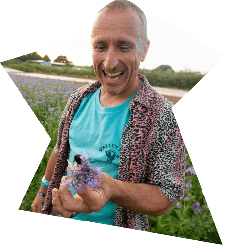A smiling Man in a ValleyFest t-shirt holds a flower while standing in a field